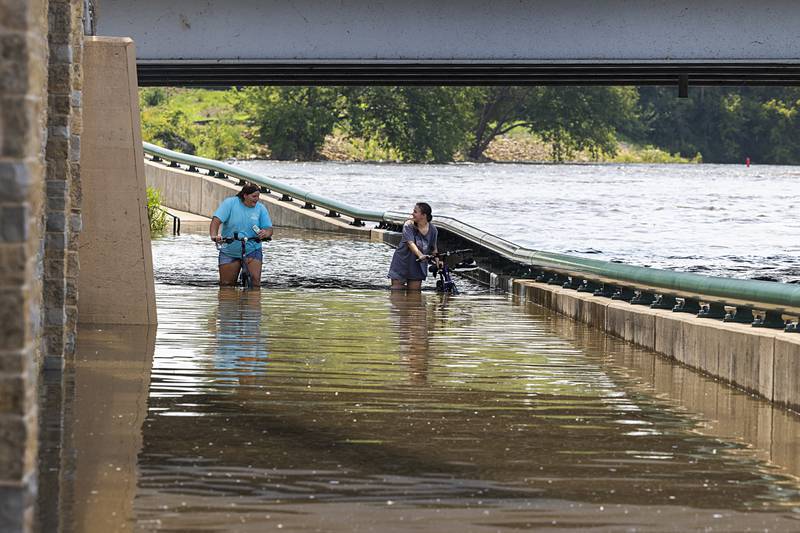 Ayla and Charlie Arellano wade through high waters below the Peoria Avenue bridge in Dixon Monday, July 15, 2024, as river levels continue to raise in the area.