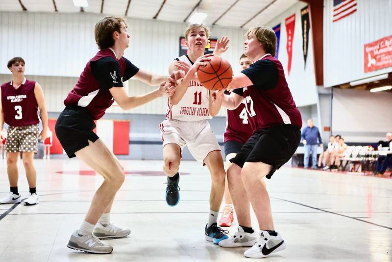 Princeton Christian Academy's Andrew Gibson drives the lane with Ottawa Christian Academy's Brody Pagakis (left), and Jackson Poggi (17) on defense Tuesday at Howard Hoffman Memorial Gym. The Eagles won 57-42.