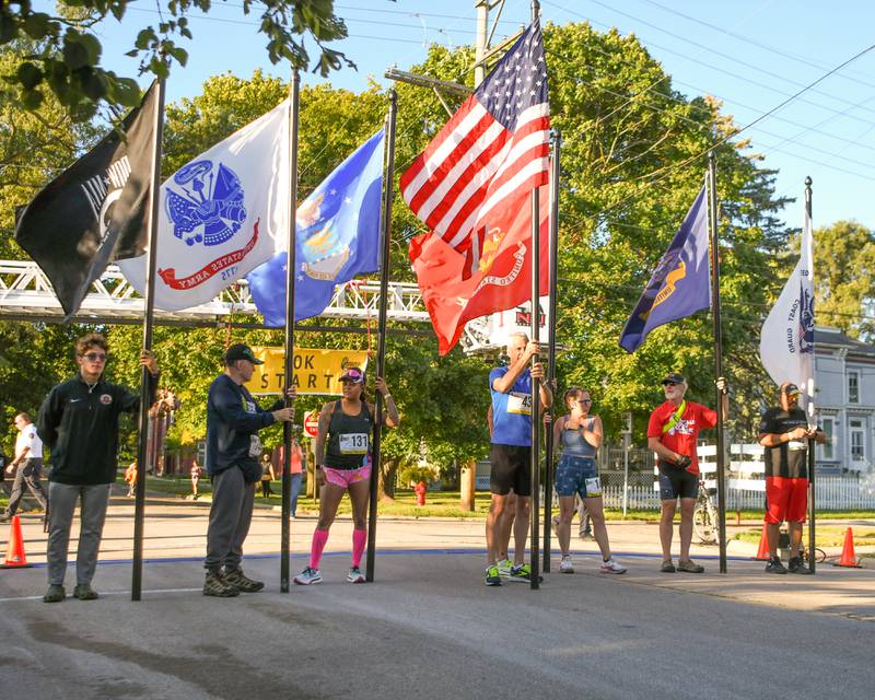 Military members who ran in the Corn Classic 5K/10K races on Sunday, Sept. 29, 2024, hold their respective branch flags before the start of the race in downtown DeKalb.