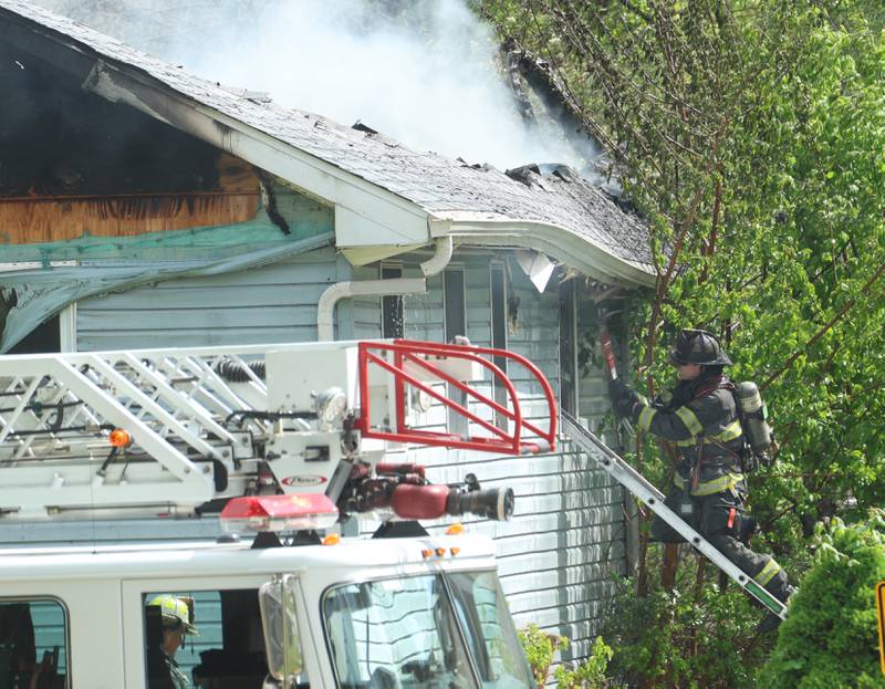 A firefighter breaks a window of a home as heavy smoke billows out from the roof in the 1900 block of Main Street on Monday, May 4, 2026 in Peru.