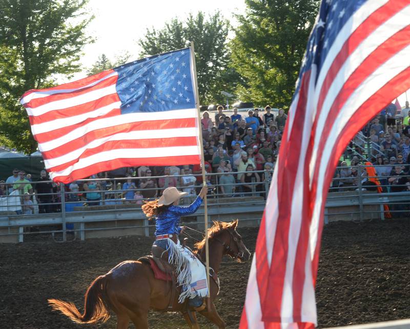 Saige McNeill of Grand Ridge carries the American flag as she rides by the reviewing stand as the National Anthem is played at the start of the rodeo at the Lee County Fair on Saturday, July 29, 2023.
