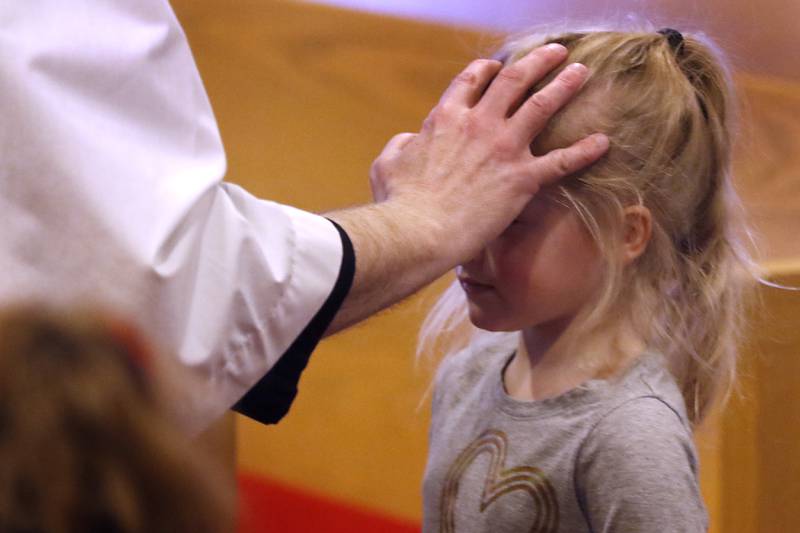Rev. Mark Buetow, of the Zion Evangelical Lutheran Church in McHenry, places ashes on a student’s forehead from the church's preschool on Wednesday, Feb, 14, 2024, during a service for the students and church members on Ash Wednesday.