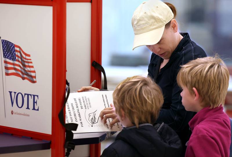 Kay Aldrich, from DeKalb, shows her kids Oliver Eich, (left) 6, and Elliott Eich, 7, the voting process Tuesday, Nov. 5, 2024, as she casts her ballot on Election Day at the DeKalb Public Library.