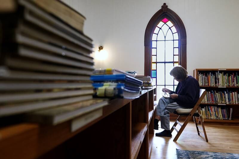 Librarian Dorothy Peterson works on adhering new stickers to the spines of books, stamping them with a "Hebron Public Library" stamp, attaching library loan cards to the inside covers, and finding a home for them on the shelves beside other books available for checkout inside the recently restored Hebron Public Library on Wednesday, April 7, 2021, in Hebron.