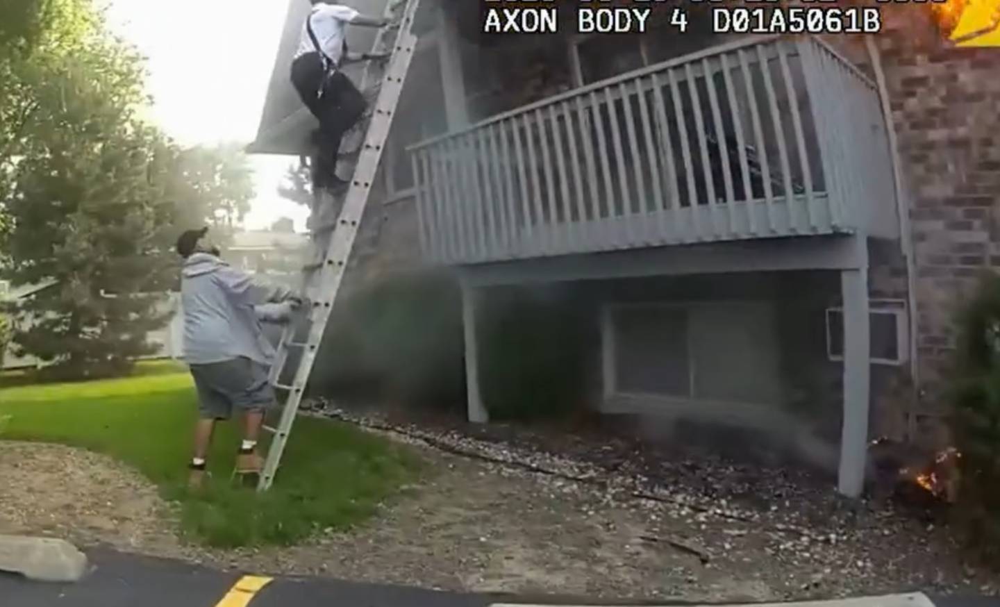 Video still showing Javier Macias, a maintenance worker, holding a ladder for Joliet Battalion Fire Chief Dan Berta as he climbs it to rescue a child and mother from an apartment fire on Tuesday, June 10, 2025, in Joliet.