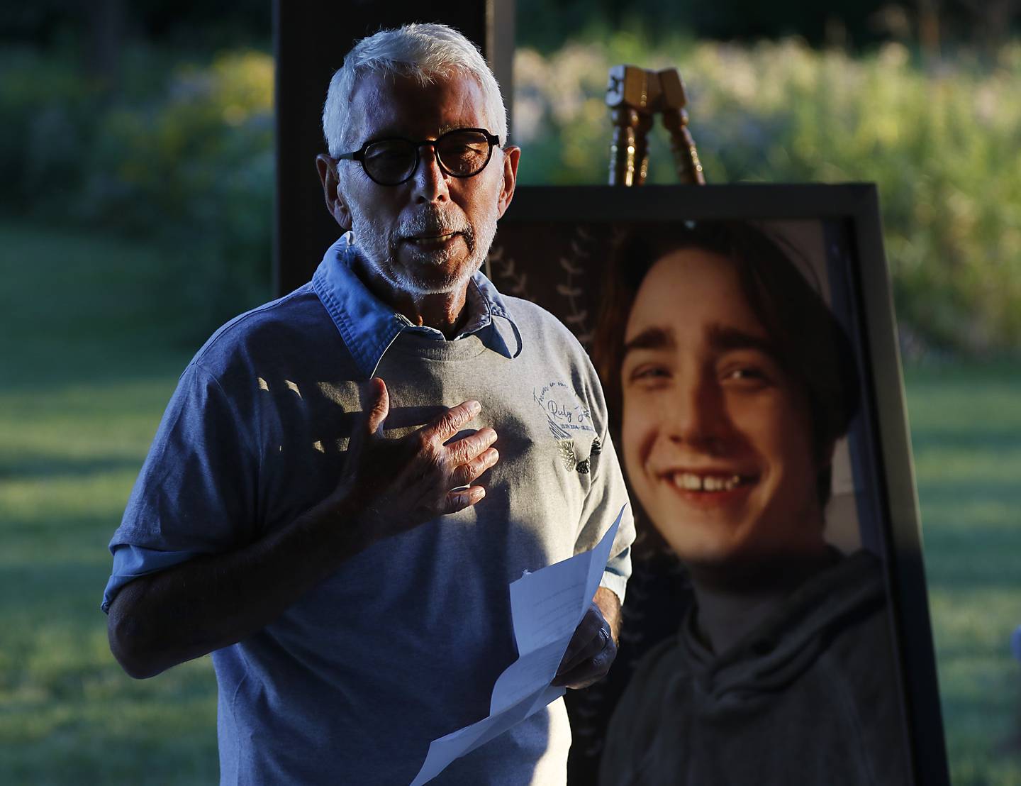 Peter Passuntino talks about his grandson, Riely Teuerle, pictured behind him, during a candlelight celebration for Teuerle on Thursday, August 11, 2022, at Towne Park, 100 Jefferson St. in Algonquin. Teuerle was killed in a car crash in Lake in the Hills the week before. Over 100 family members and friends gathered at the park to remember and celebrate Teuerle’s life.