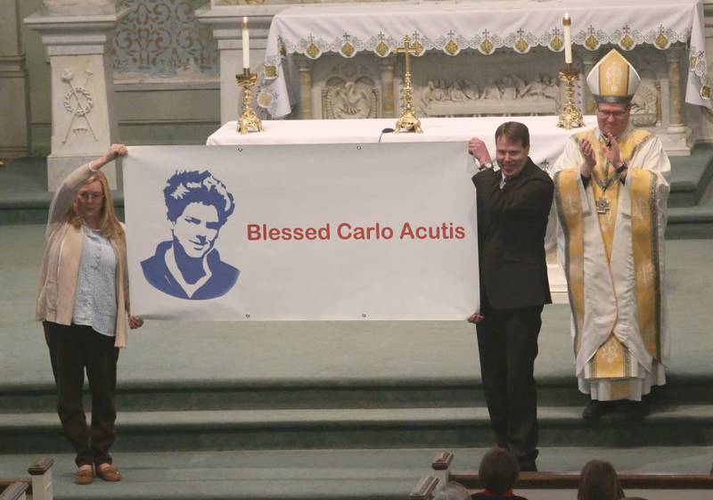 (From left) Dr. Susie Cicciarelli Office of Catholic Schools, Associate Superintendent, Nathan Boudreau, Principal at Holy Family School in Oglesby and The Most Reverend Bishop Louis Tylka, Bishop of Peoria unveil the banner of the new consolidated school name of Carlo Acutis during an All Schools Mass on Thursday, Feb. 20, 2025 at St. Patrick's Catholic Church in La Salle. Last year, the Catholic Diocese of Peoria announced the consolidation of the three schools. Carlo Acutis Canonization will take place on Sunday, April 27, 2025 during the Jubilee of Teenagers in Rome. Acutis is the first millennial saint, representing those born between the early 1980's and the late 1990's. He is celebrated for cataloging miracles and online and managing websites for Catholic organizations.