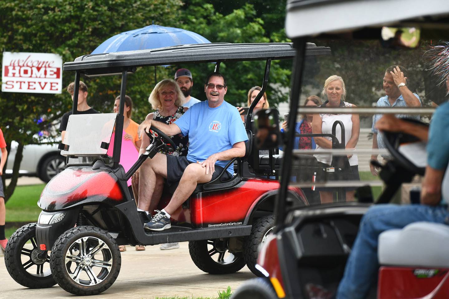 A welcome home parade drives past Steve Schultz on July 1, 2022, as he sits in his driveway for the first time in 208 days after returning home from battling COVID-19. His wife, Cathy, children and family surrounded him as neighbors and friends lined the streets.