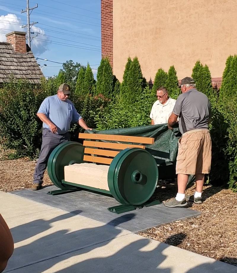 Steve Benesh's sons, Tim (left) and Tony (right) unveil the bench with Mike Bowers pictured behind the bench. The unique bench is located in John Phelps Park, west of the Oregon Coliseum in downtown Oregon.
