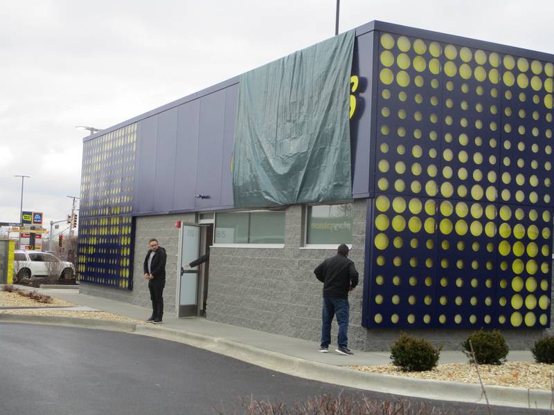 Men in dark coats seen stepping outside of what is believed to be McDonald's future CosMc's restaurant in Bolingbrook. Tarp covers the CosMc's signage on the building wall. Dec. 2, 2023.