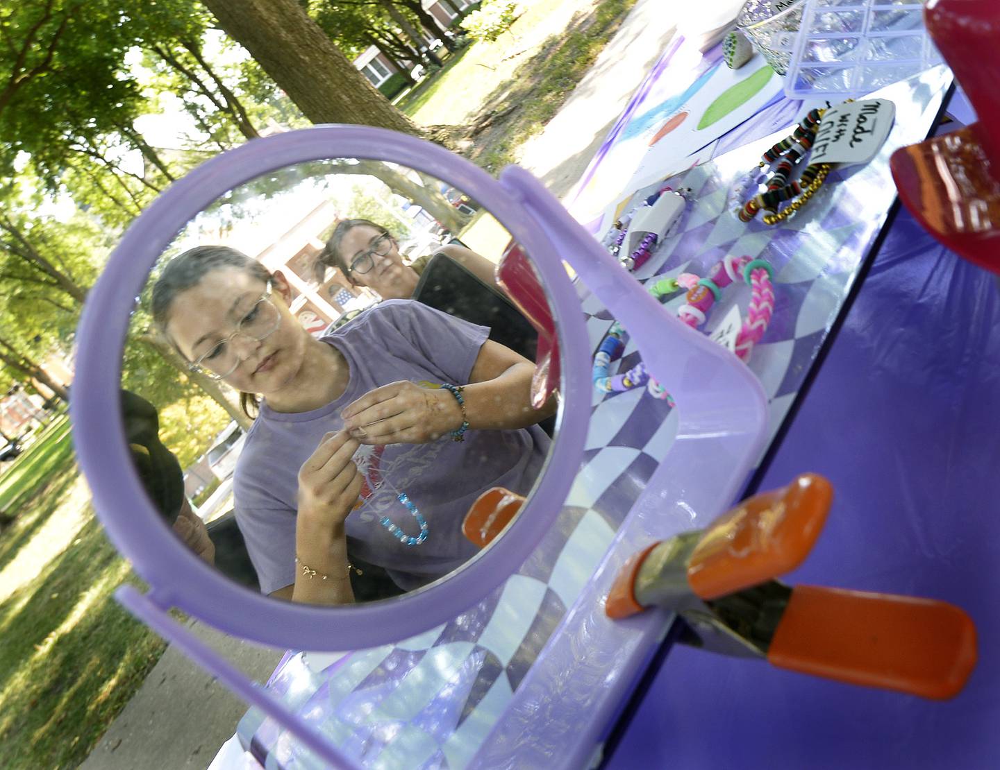 Reflected in a mirror, Moira and Maddie Grenda, works bracelets at their table Saturday at Washington Park in Ottawa during the 4th annual Children’s Business Fair sponsored by Prairie Fox Books.