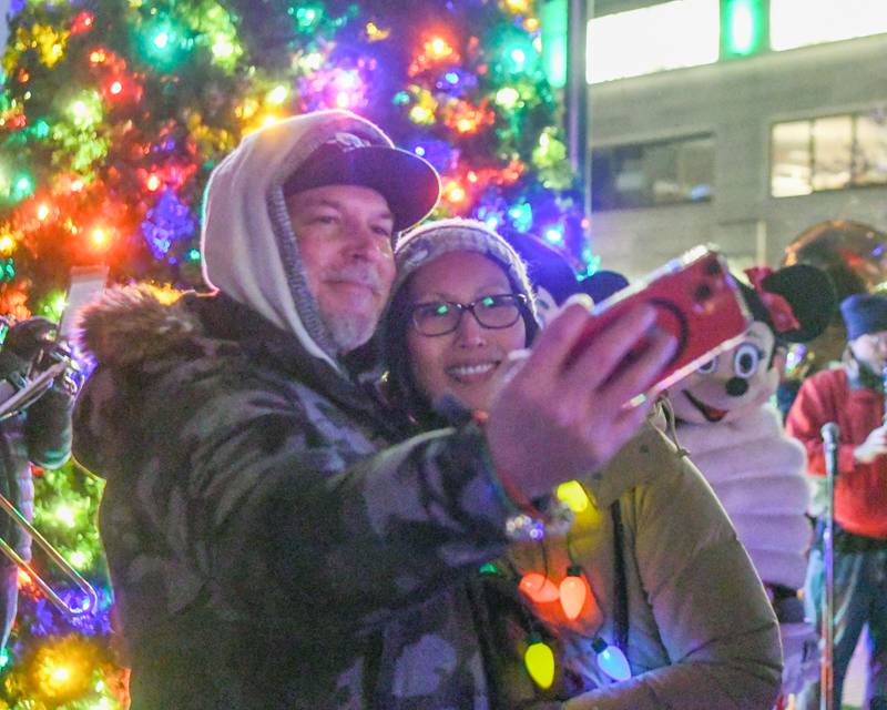 Doug and Jaena Stanley from St. Charles who run alphagraphics in Wheaton and sponsored Micky and Minnie, take a selfie in front of the tree after the holiday parade in downtown Wheaton on Friday Nov. 24, 2023.