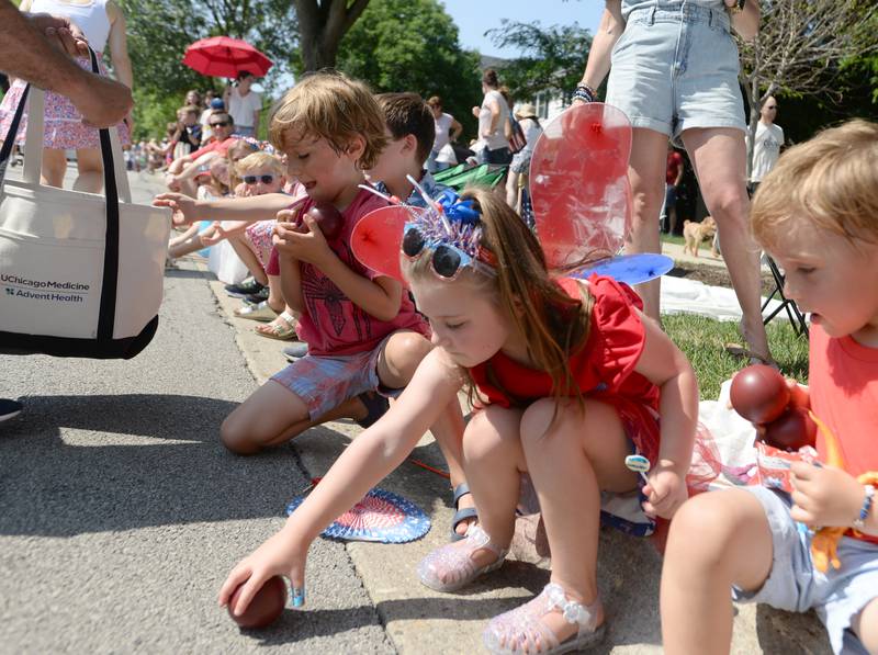 (Children including Izzy Laux of Hinsdale collect candy and footballs thrown to them during the Hinsdale 4th of July parade Tuesday June 4, 2023.