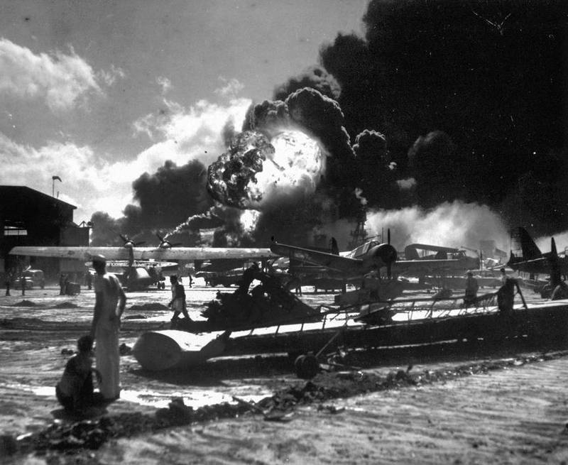 In this Dec. 7, 1941, photo provided by the U.S. Navy, sailors stand among wrecked airplanes at Ford Island Naval Air Station as they watch the explosion of the USS Shaw, background, during the Japanese surprise attack on Pearl Harbor, Hawaii. More than 2,300 U.S. service members and civilians were killed in the strike which brought the United States into World War II.