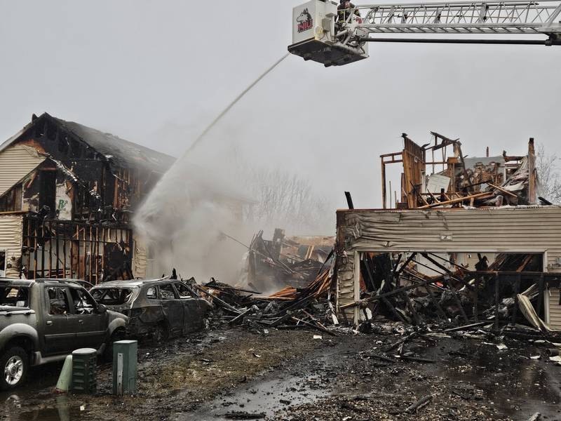 Crews use a fire hose from the DeKalb Fire Department's ladder truck to battle a multi-home fire in the early morning hours on Sunday, March 16, 2025, in the 200 block of Market Street in the Riverbend Subdivision in Genoa.