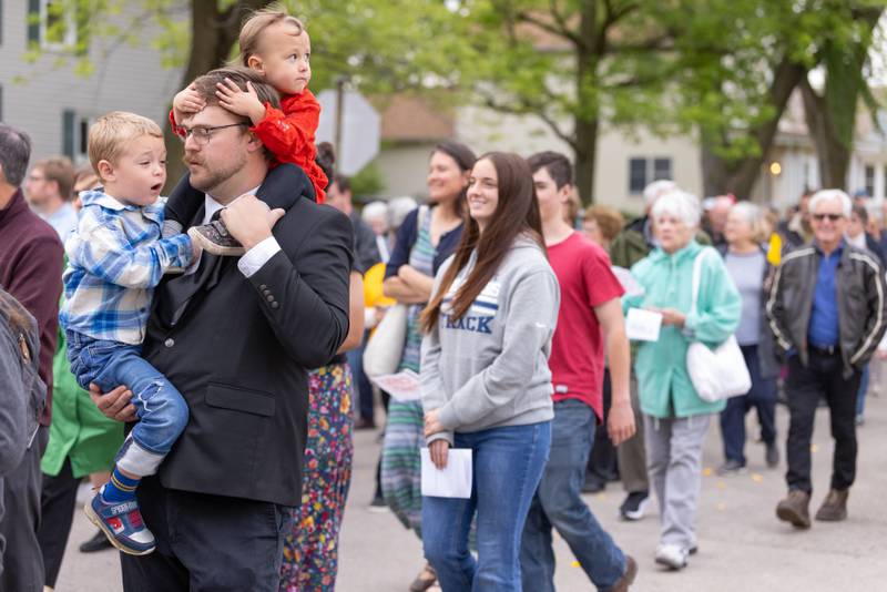Michael Templeton Jr. carries his two children in a procession from St. Hyacinth Church to the Queen of the Holy Rosary Shrine on May 19, 2025, in La Salle.