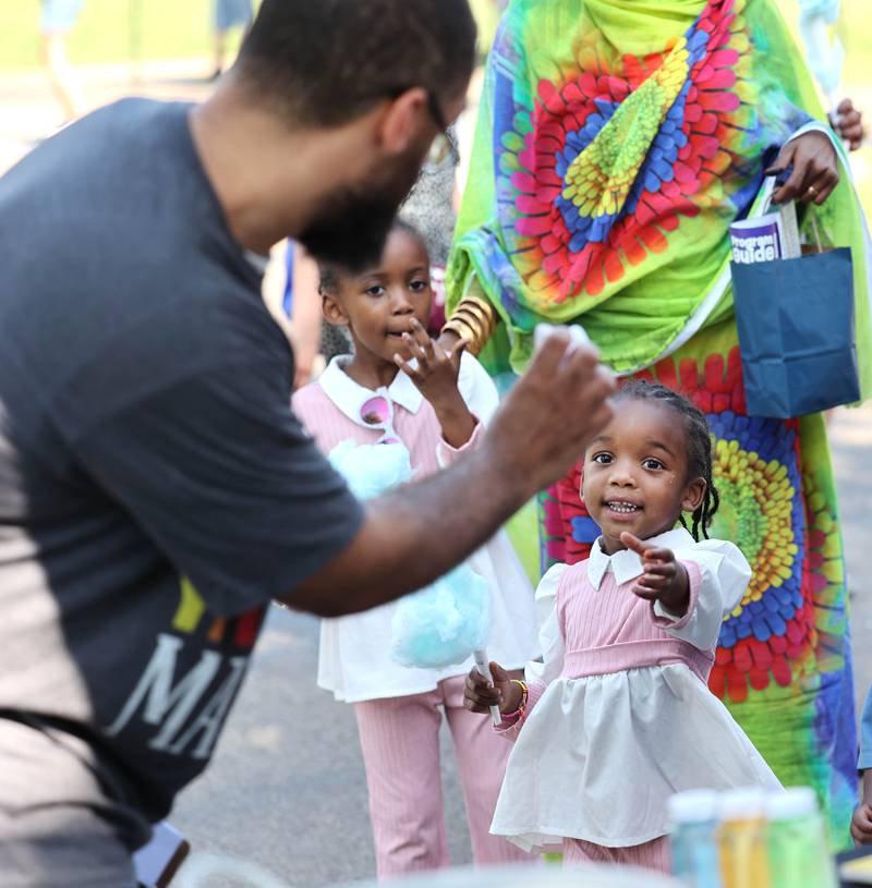 Matab Bagal, 3, from Inderoy, Norway, picks up some free goodies at one of the booths during the Family Fun Fest Thursday, July 20, 2023, at Hopkins Park in DeKalb.