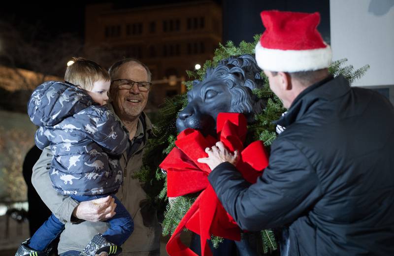 Elliot McHugh, 3, of Chebanse, left, assists Kankakee Mayor Chris Curtis, right, lay the holiday wreaths on the lion statues outside the Kankakee Library on Thursday, December 4, 2025.