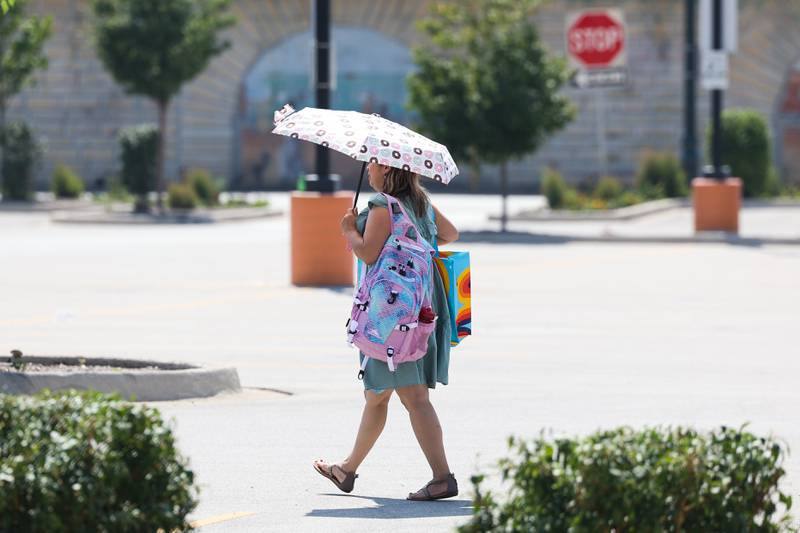 A pedestrian uses an umbrella for shade as the heat index hits triple digits on Thursday, Aug. 24, 2023 in Joliet.