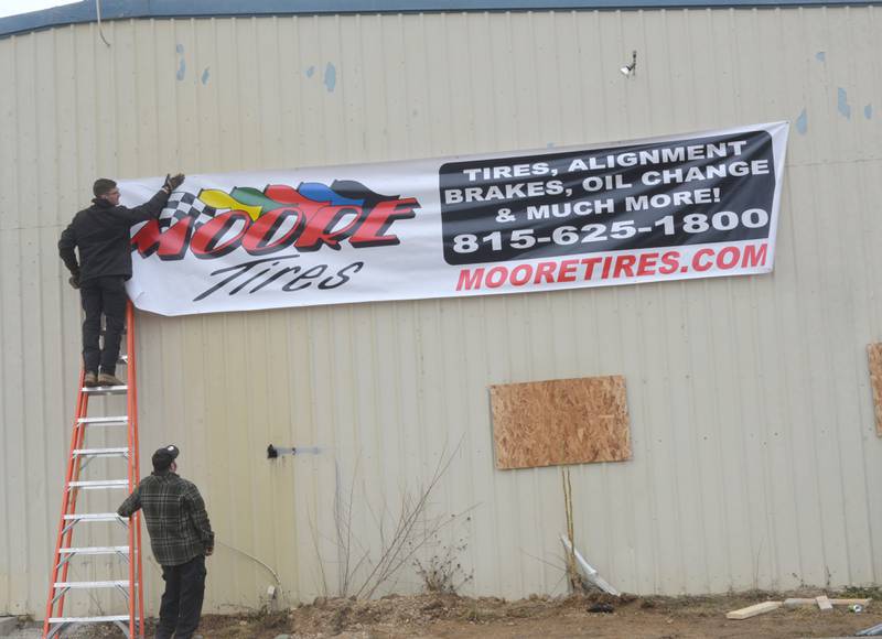 Kyle Moore and Todd Billings secure a Moore Tires banner to the business' new location on Tuesday, Feb. 6, 2024.