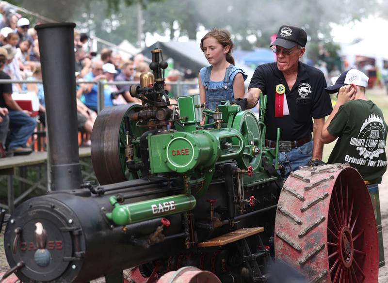 Evalynn Chapman, 8, from Oregon, steers a Case half scale steam engine through the parade with a little help from her grandpa Dave Stevens, from Sycamore, Thursday, Aug. 7, 2025, at the 68th annual Sycamore Steam Show and Threshing Bee at Taylor Marshall Farm on Lukens Road in Sycamore.