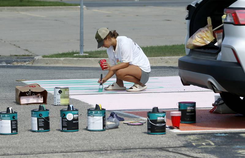 Painter Payton Walsh paints tulips on butterflies on Summer Hertal’s parking spot on Tuesday, Aug. 13, 2024, at Marian Central High School in Woodstock.