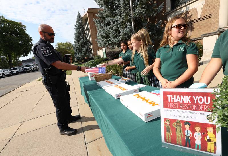 Bishop McNamara Catholic School fifth grader Allie Quigley hands a thank you card and an American flag made by kindergarteners to Bradley Police Officer Matt Baxter as she and her fellow student council members host the 10th Gratitude Drive-Thru for first responders and military members on Thursday, Sept. 11, 2025.