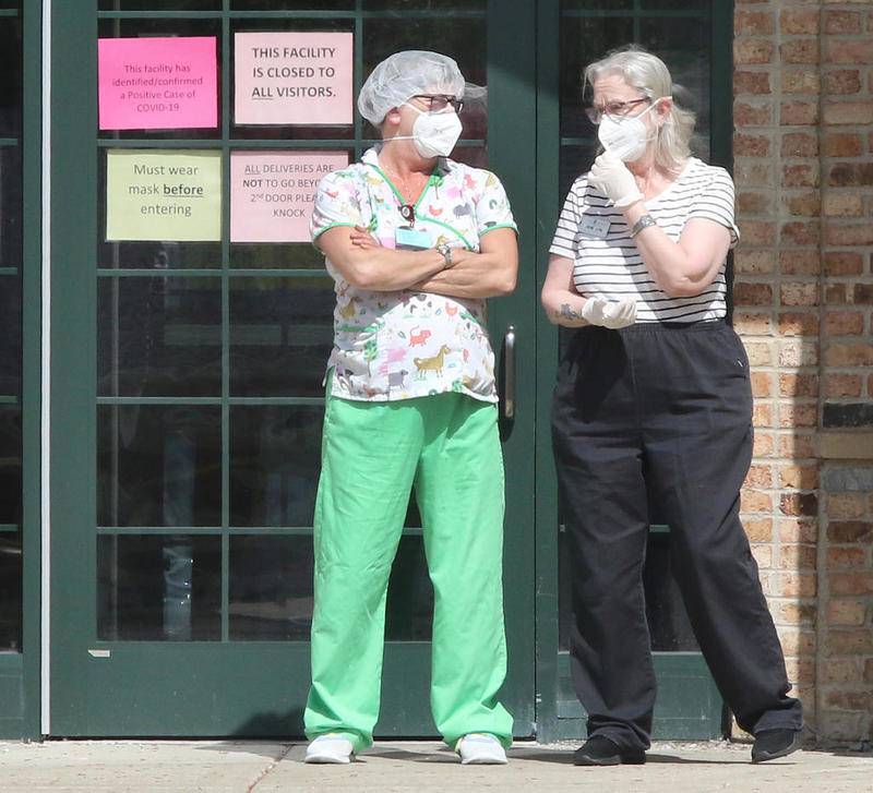 Two people talk outside the front entrance of Pine Acres Rehab and Living Center in DeKalb Thursday afternoon as signs posted on the door warn that there are confirmed cases of COVID-19 in the building. Nine staff members and 31 residents at the facility have tested positive for COVID-19. One resident has died as a result of complications from the disease.