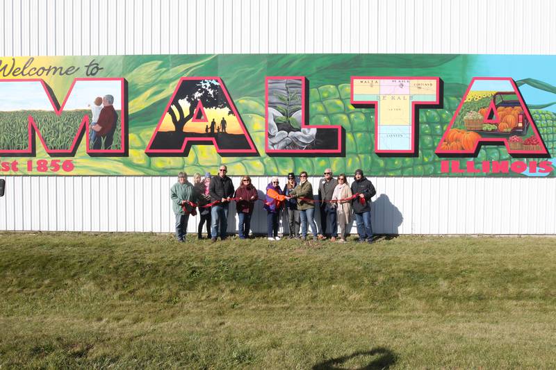 The ribbon is cut by Malta city officials and other people responsible for completing the project including Dixon artist Nora Balayti and building owner Shirley Kyler Wednesday, Oct. 19, 2022, on the north side of Route 38 in Malta. The mural, which spells out Malta in large capital letters, depicts the values of the town with themes of agriculture, family, community and growth.