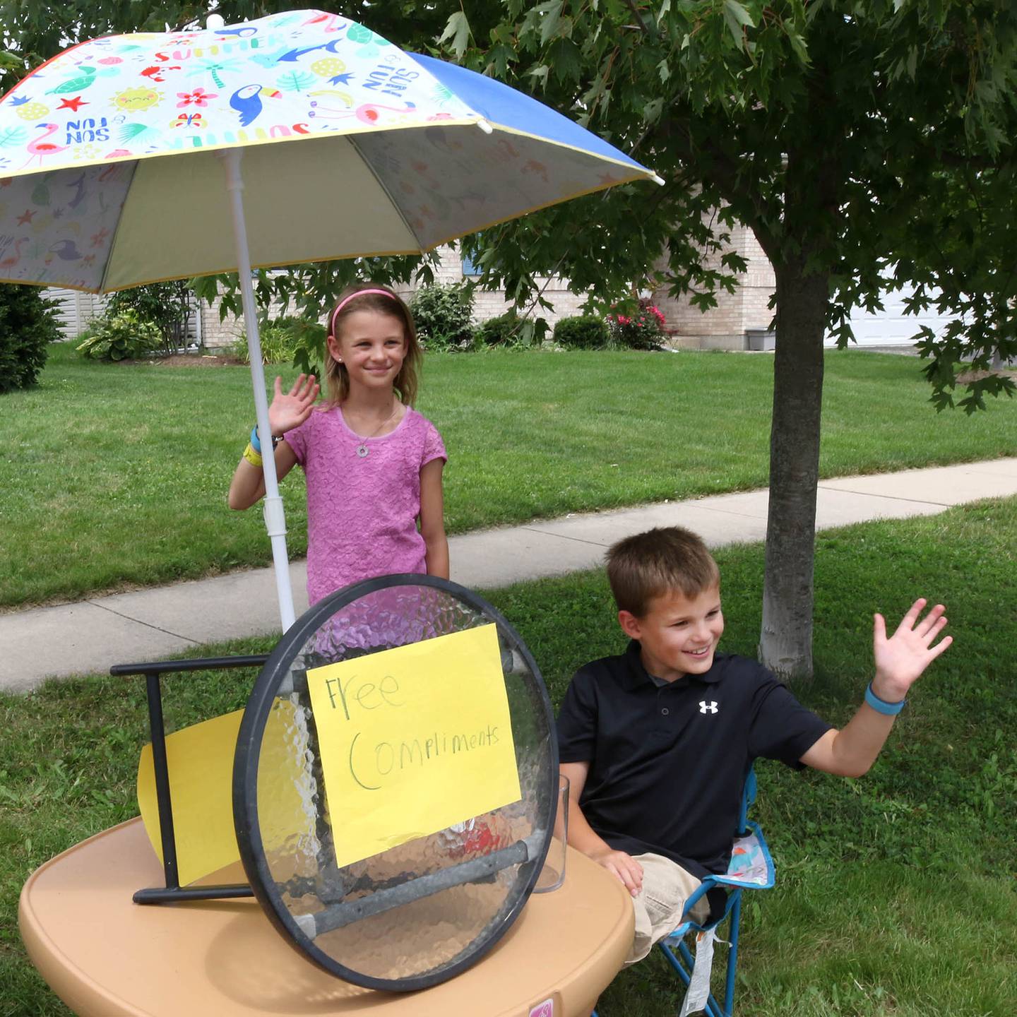Ethan Wargo, 9, and his twin sister Claire wave to a passing motorist Thursday, July 24, 2025, at the free compliments stand in front of their house in Sycamore. Ethan offers free compliments to anyone who stops by but he said tips are accepted and appreciated.
