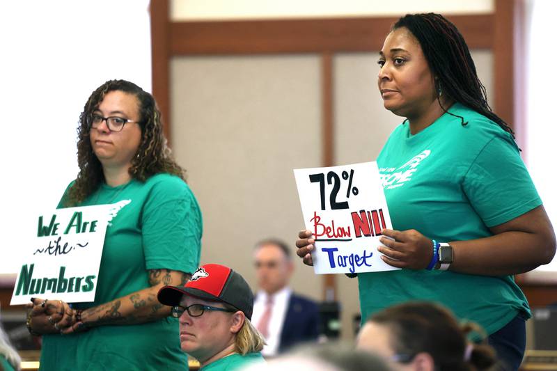Northern Illinois University employees stand up and hold signs Thursday, June 12, 2025, during the NIU Board of Trustees meeting in Altgeld Hall at NIU in DeKalb. NIU clerical, professional and administrative workers represented by the American Federation of State, County and Municipal Employees Local 1890 are asking for higher wages when their contract expires at the end of the month.