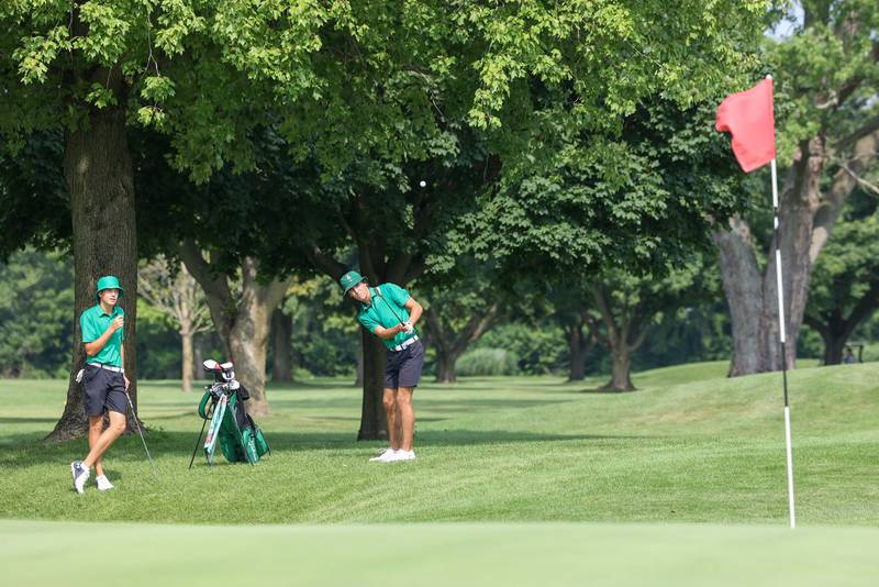 Bishop McNamara's Preston Payne, right, chips toward the green as teammate Griffin Meier looks on during the Bill Breeden All-Area Classic at the Kankakee Elks on Monday, Aug. 18, 2025. Payne scored a 97 as Meier scored a 91 to help earn Bishop McNamara fourth place overall.