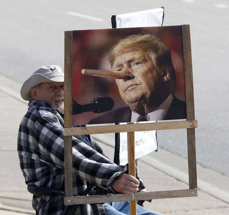 Gary Perrine holds a picture of President Donald Trump as he protests near the intersection of McCullom Lake Road and State Route 31, in McHenry on Saturday, March 28, 2026, during the McHenry County No Kings Protest. According to an organizer, over 4,000, people took part in the protest.