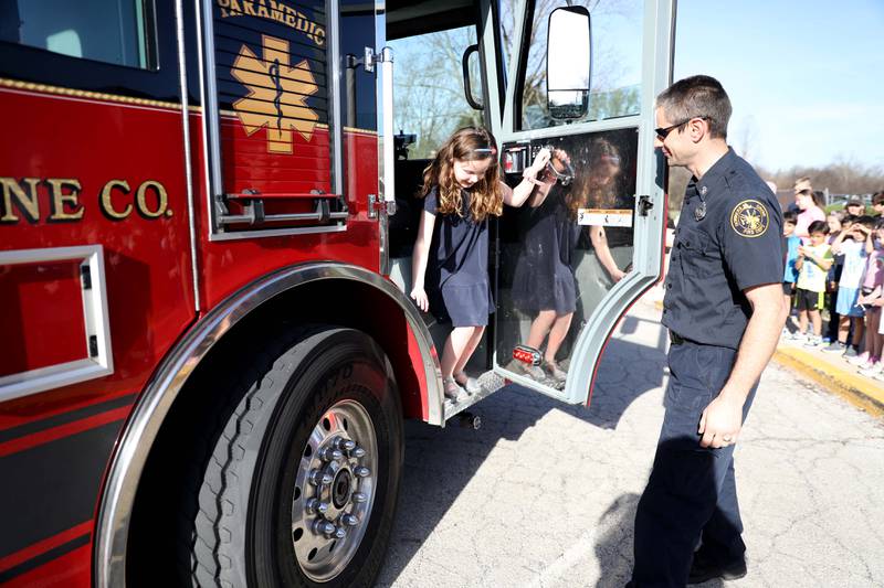 Belle Aire Elementary School third-grader Kyla Richardson hops out of a Downers Grove Fire Department truck with the help of firefighter/paramedic Kris Nowak on Thursday, April 13, 2023. Kyla won the trip by entering a contest sponsored by the  Fire Department as part of the Learn Not to Burn program.