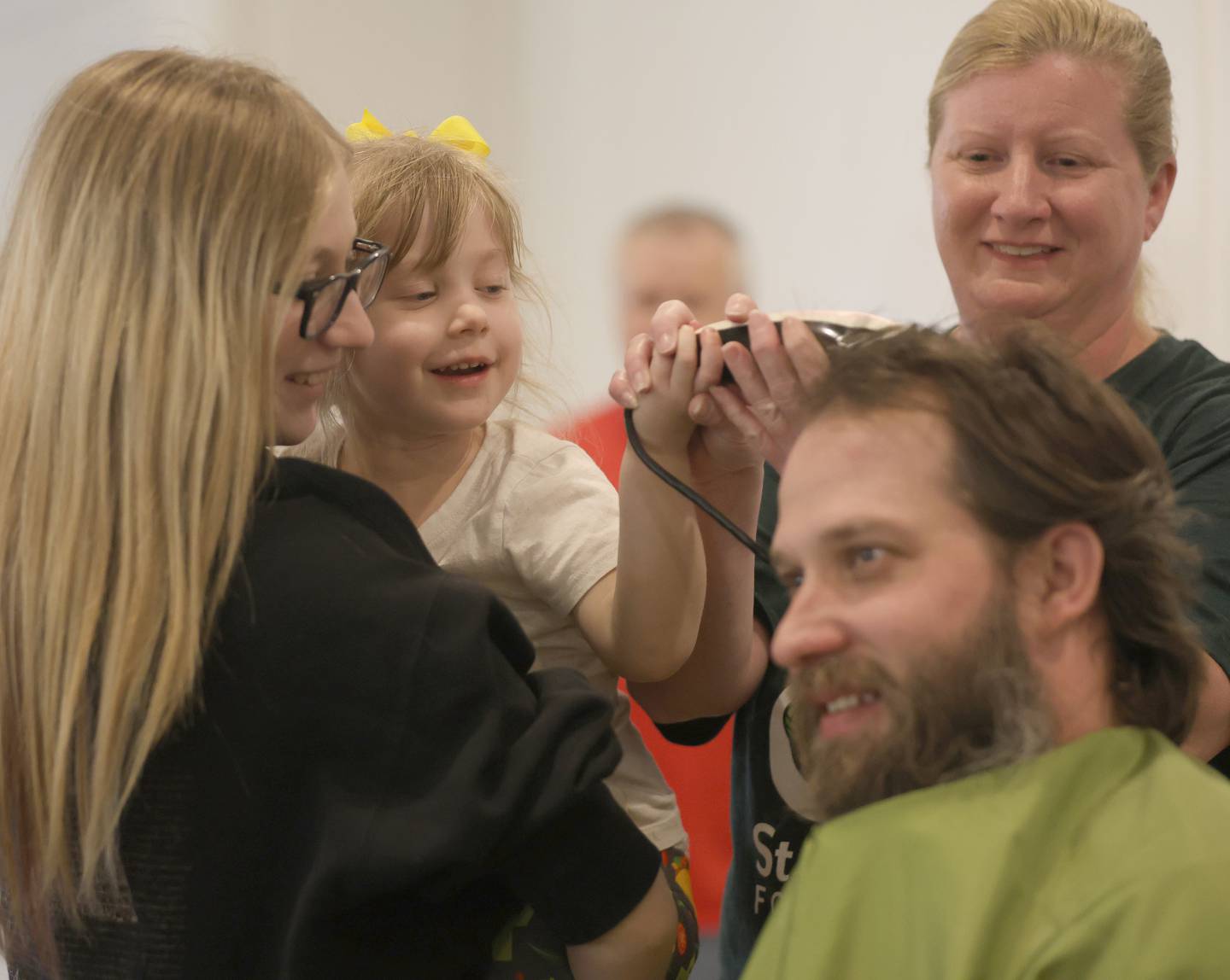 Avery Hamilton holds her sister Delaney as they take their first swipe of hair on their John with the help of beautician Sarah Paytak of Downstairs of First Day Spa during the 19th annual Illinois Valley Emergency Services Annual St. Baldrick's Event on Sunday, March 22, 2026 at Senica's Oak Ridge in La Salle.