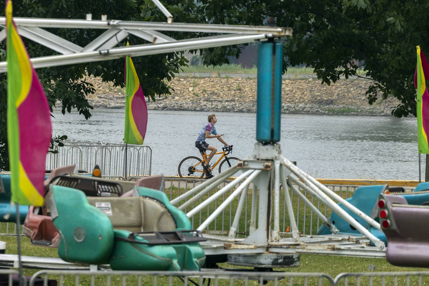 A bicyclist rides the path past Petunia Fest carnival rides in Dixon Monday, June 26, 2023.