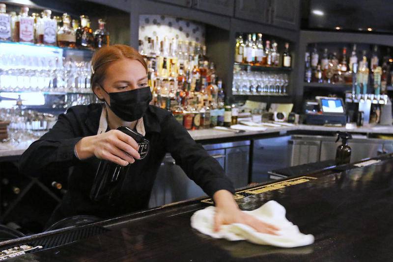 Bartender and server Brittany Crane prepares for the dinner rush Wednesday by performing cleaning tasks such as wiping down the bartop with a sanitizing solution at 1776 Restaurant in Crystal Lake. The restaurant is one of many local businesses that will have to adapt again to new COVID-19 safety guidelines in order to remain open for business.