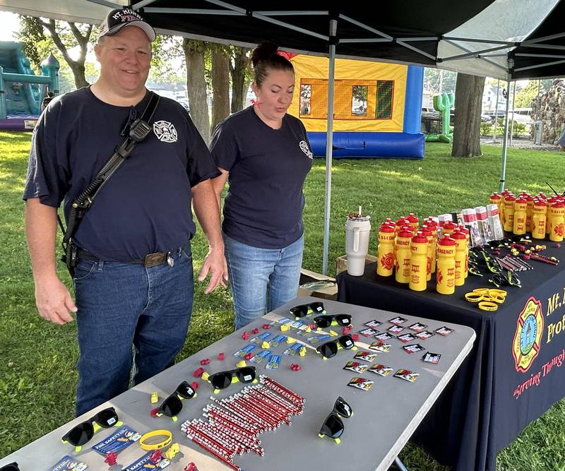 Mt. Morris Fire Chief Rob Hough iV and EMT Amber Hoffman stand behind the fire department's merchandise table at the National Night Out event in Mt. Morris on Tuesday, Aug. 5, 2025.