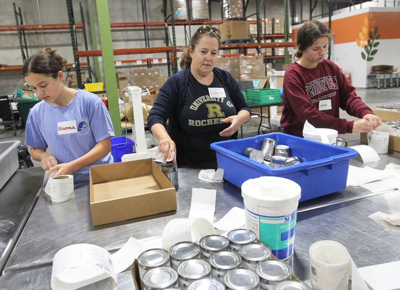Suzanne Sands, of Lake Forest (center) works with her daughters, Hanna, 17, and Emma, 13, labeling cans of vegetables at the Northern Illinois Food Bank on August 19th in Lake Forest. The North Suburban Center recently celebrated it’s one-year anniversary at this location.  
Photo by Candace H. Johnson for Shaw Local News Network
