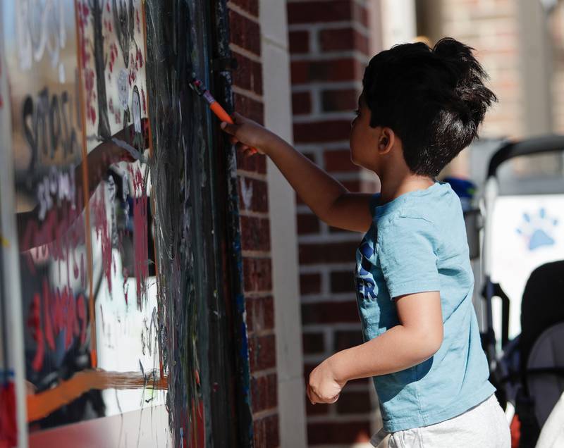 Krishna Elkin, 4, of Naperville paints the windows of a business in Downers Grove, Ill. on Saturday, October 22, 2022.