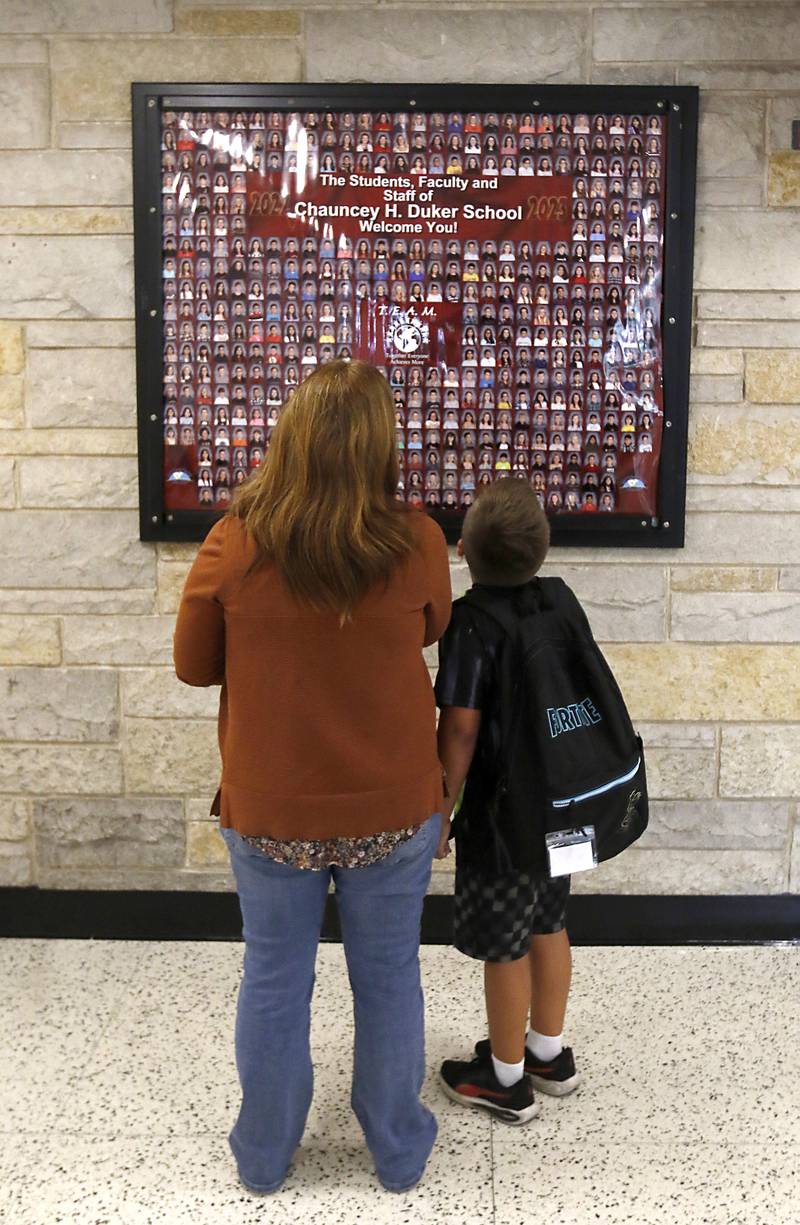 Logan Nienaber, and his mother, Laura Kram looks at a picture of students and teachers on Tuesday, Aug. 15, 2023, during school supplies drop-off day at Duker Elementary School in McHenry.