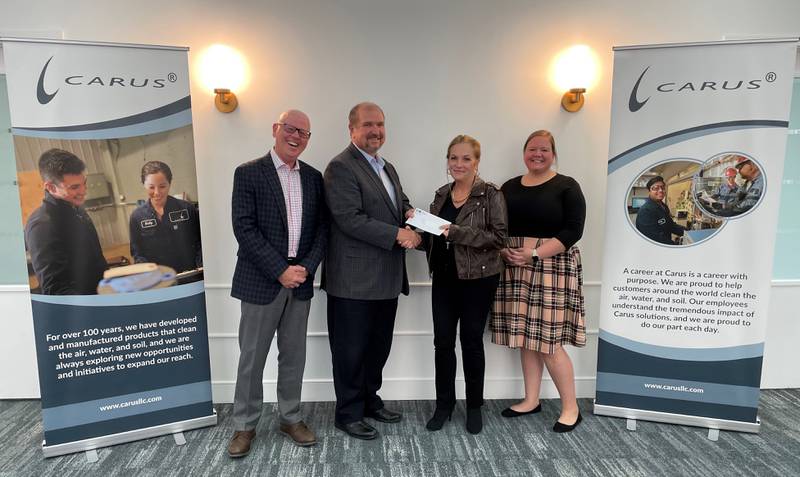 Randy Prince, a representative from the Illinois Manufacturers Association (second from left), presents a check to Andy Johnston, Chryss Crockett and Bailee Wallace of Carus LLC (from left to right).