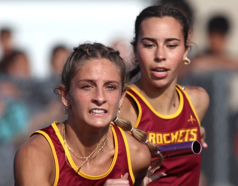 Richmond-Burton’s Kristina DeLeon, right, hands the baton to teammate Sophia Komar  in the 400-meter relay during the McHenry County Track and Field Meet at McCracken Field on Thursday, April 24, 2025, in McHenry
