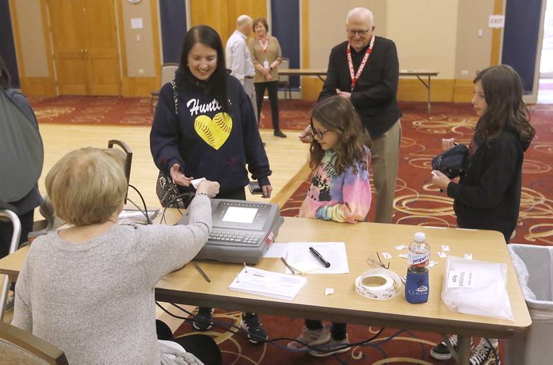 Election judge Sharon Lynch hands Katie Hoving of Hampshire her ballot information on Tuesday, April 4, 2023, during in the 2023 consolidated election at Del Webb Sun City’s Prairie Lodge in Huntley. Hoving, brought along her daughters Alexa, 7, and Julia, 11.