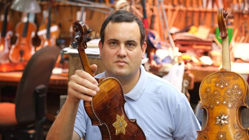 Avshi Weinstein, co-founder of Violins of Hope, is pictured with a Holocaust era violin he has restored in his workshop in Israel. CREDIT: Amnon Weinstein.