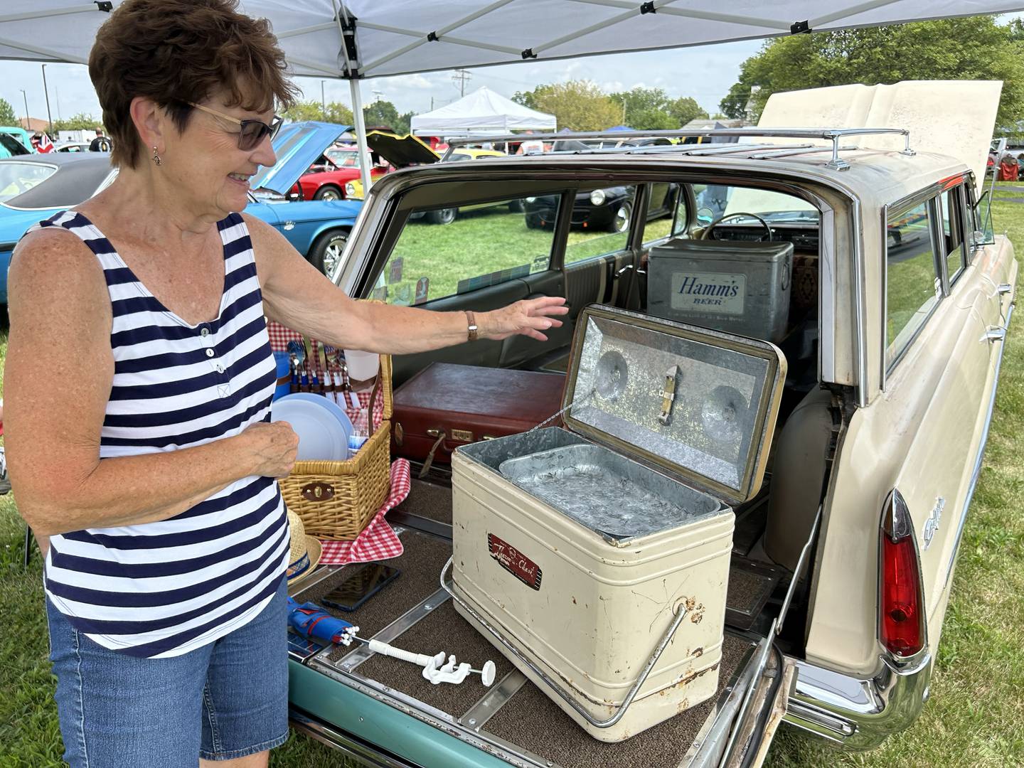 Dave and Shelia Dean brought their 1961 Pontiac Bonneville Safari station wagon to the Hib Reber Memorial Car Show held during ByronFest on Saturday, July 13, 2024 in Byron. Here, Sheila points to the bottle opener in the lid of. vintage cooler that was part of the couple's display.