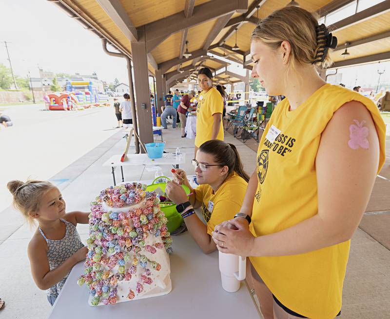 Emmie Farnham, 5, picks a sucker from BLIND leaders Leah Kalina (left) of Newman and Mayson Burns of Rock Falls Friday, August 4, 2023. Leaders for the program Building Lasting Impressions that Never Die spent the day in Sterling running a family fun fair, washing cars and helping out at Hot Dog Days.