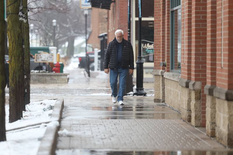 A pedestrian walks the wets sidewalk along Des Plaines Street in downtown Plainfield as morning snow turned to afternoon rain on Tuesday, Jan. 9th, 2024.