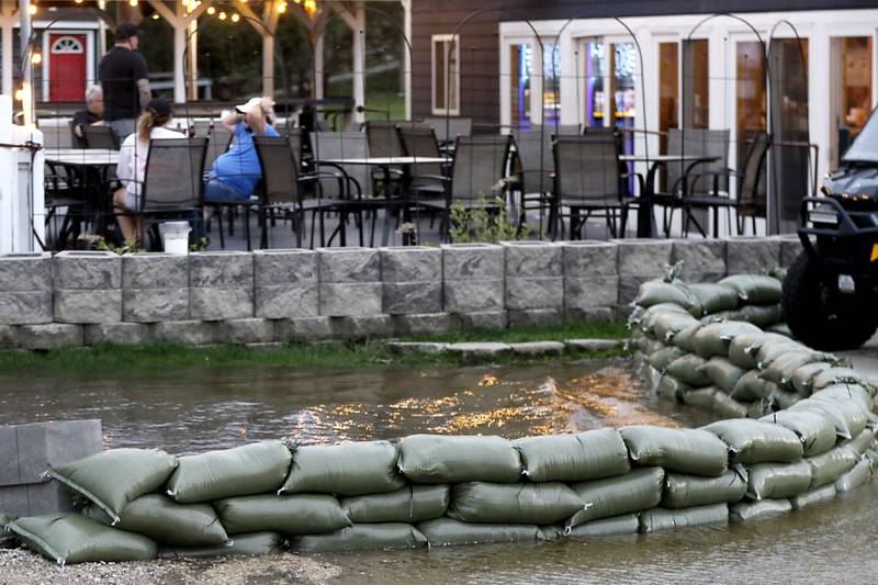 People hang out on the deck of the Bru Crew Bar and Grill as sandbags line the boat ramp area next to the restaurant on Friday, April 17, 2026, in Johnsburg.