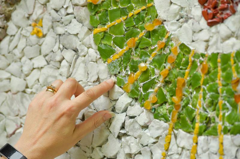 Volunteer Valerie Taylor glues on tinny colored stones in one of the mosaics as part of the restoration work on the Geneva Grotto on Thursday, June 15, 2023.